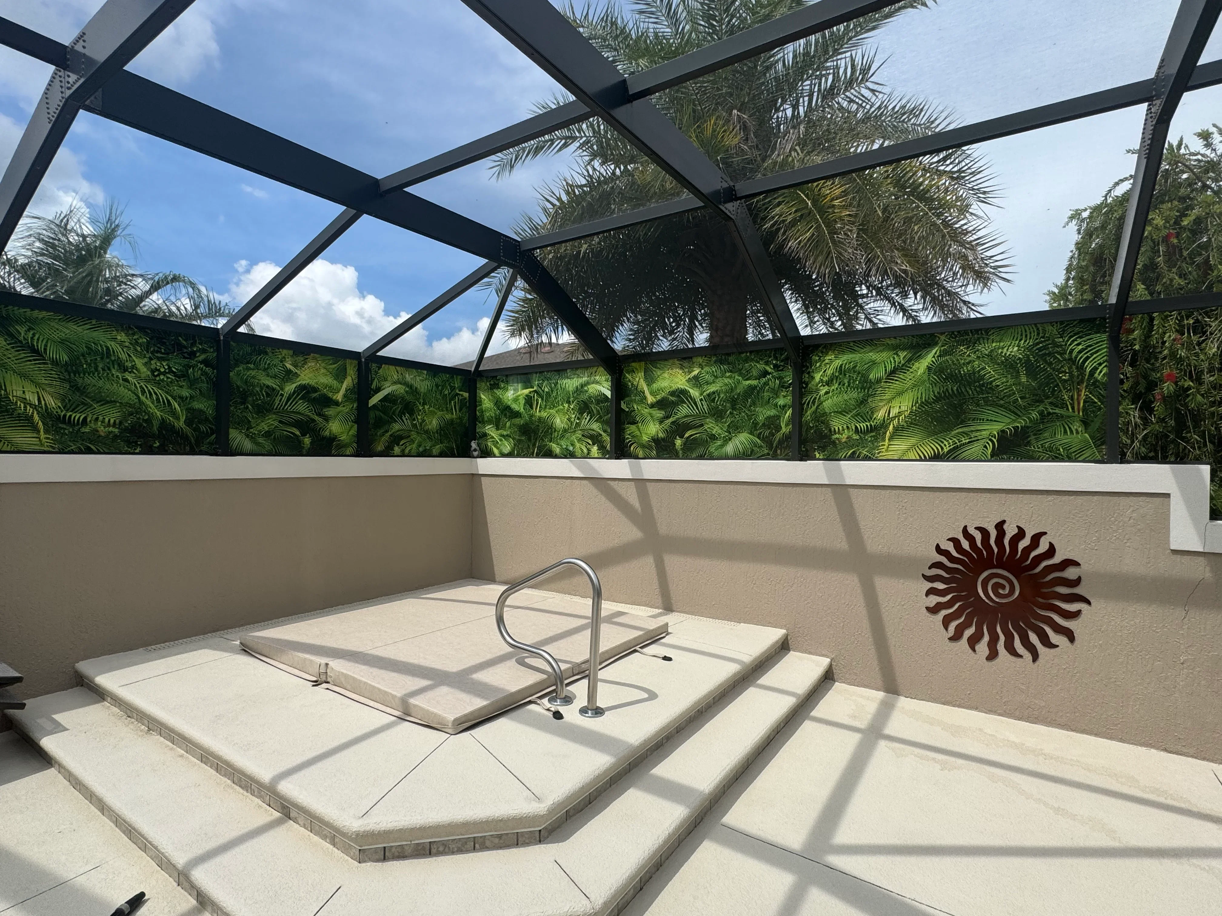 Black aluminum screen enclosure with gable roof, concrete spa deck, and tropical plant backdrop