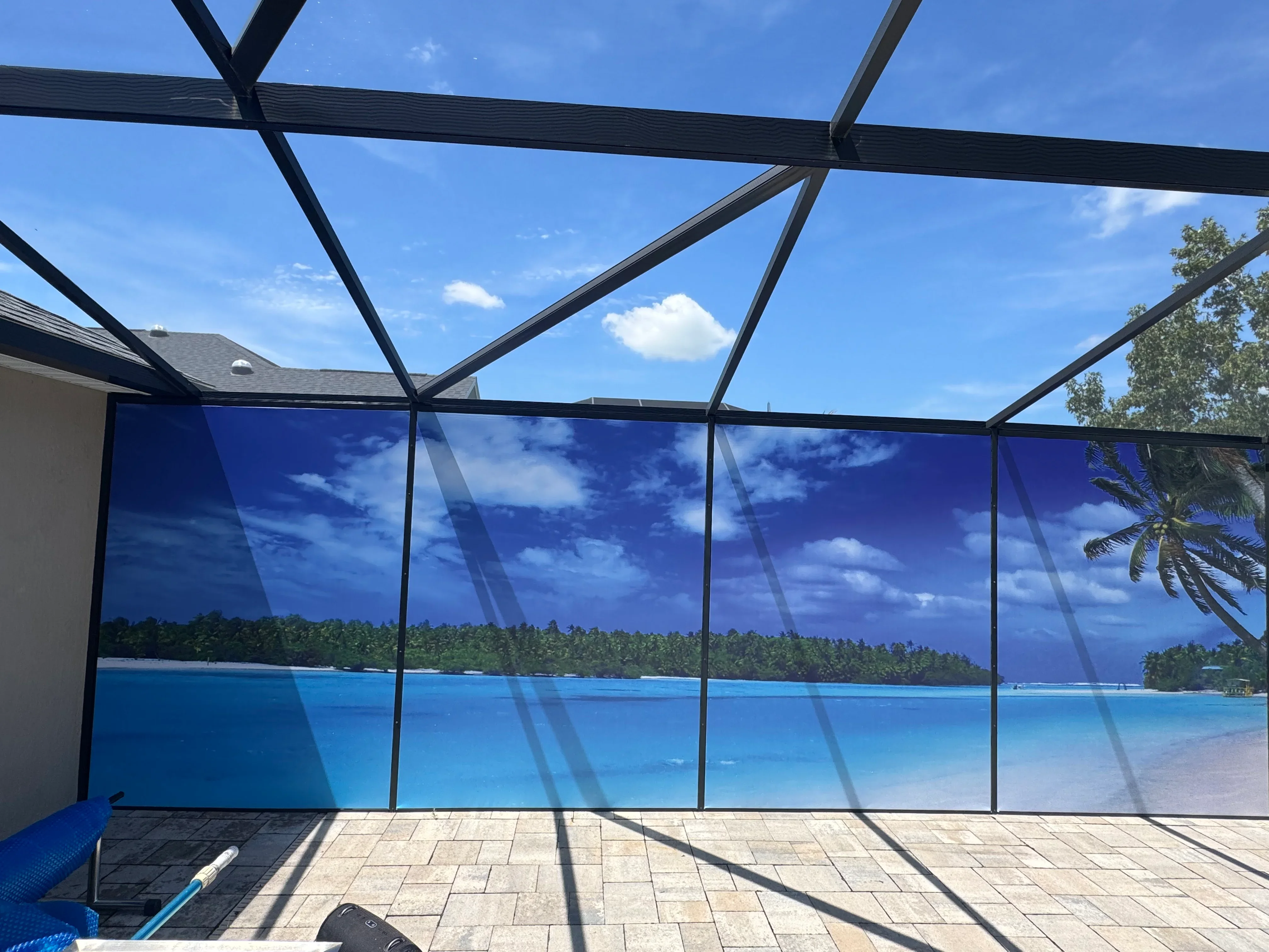 Black aluminum screen enclosure with glass panels and overhead pergola frame on paver patio