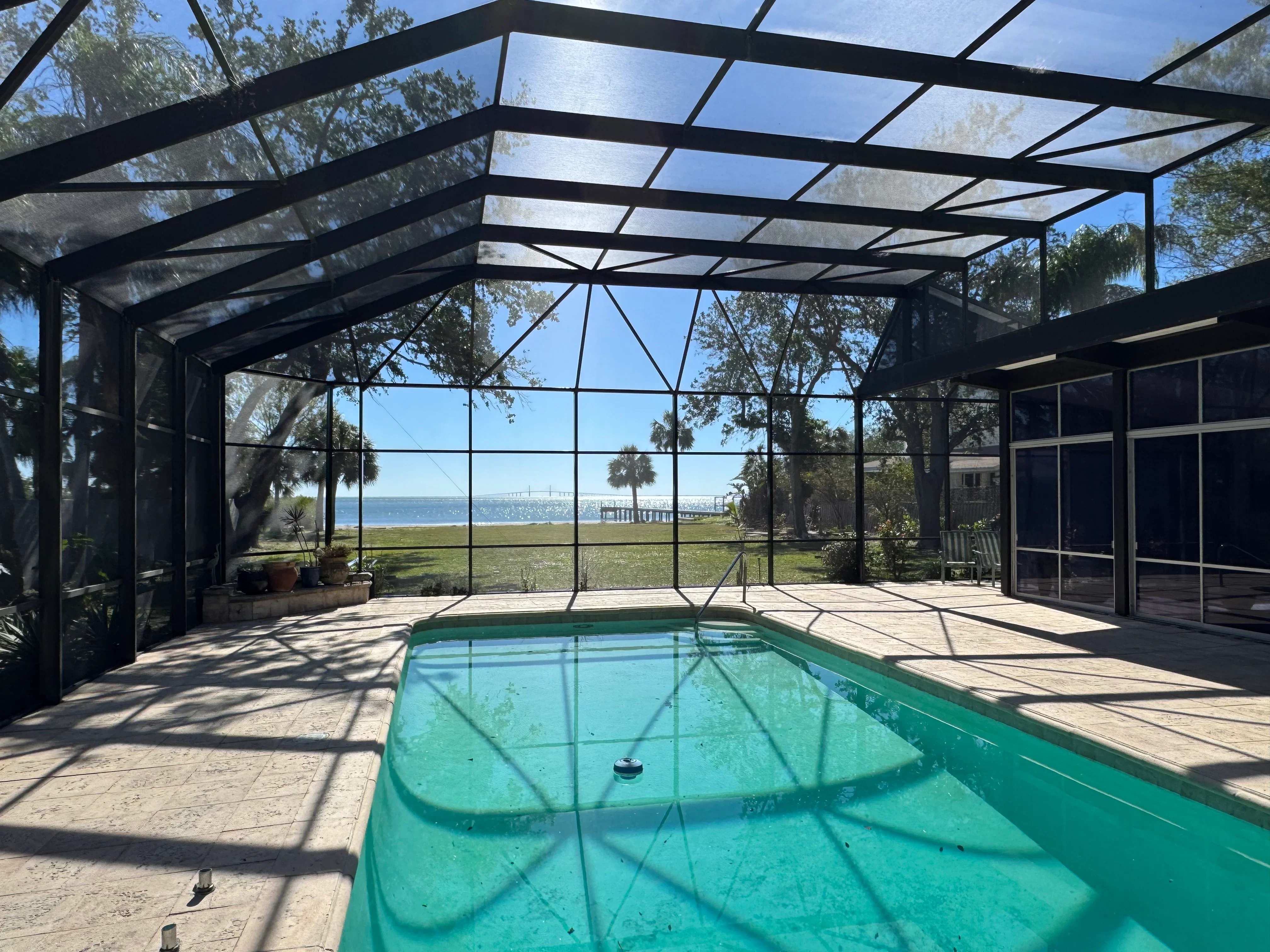 Black aluminum pool enclosure with clear panels overlooking waterfront, turquoise pool water visible
