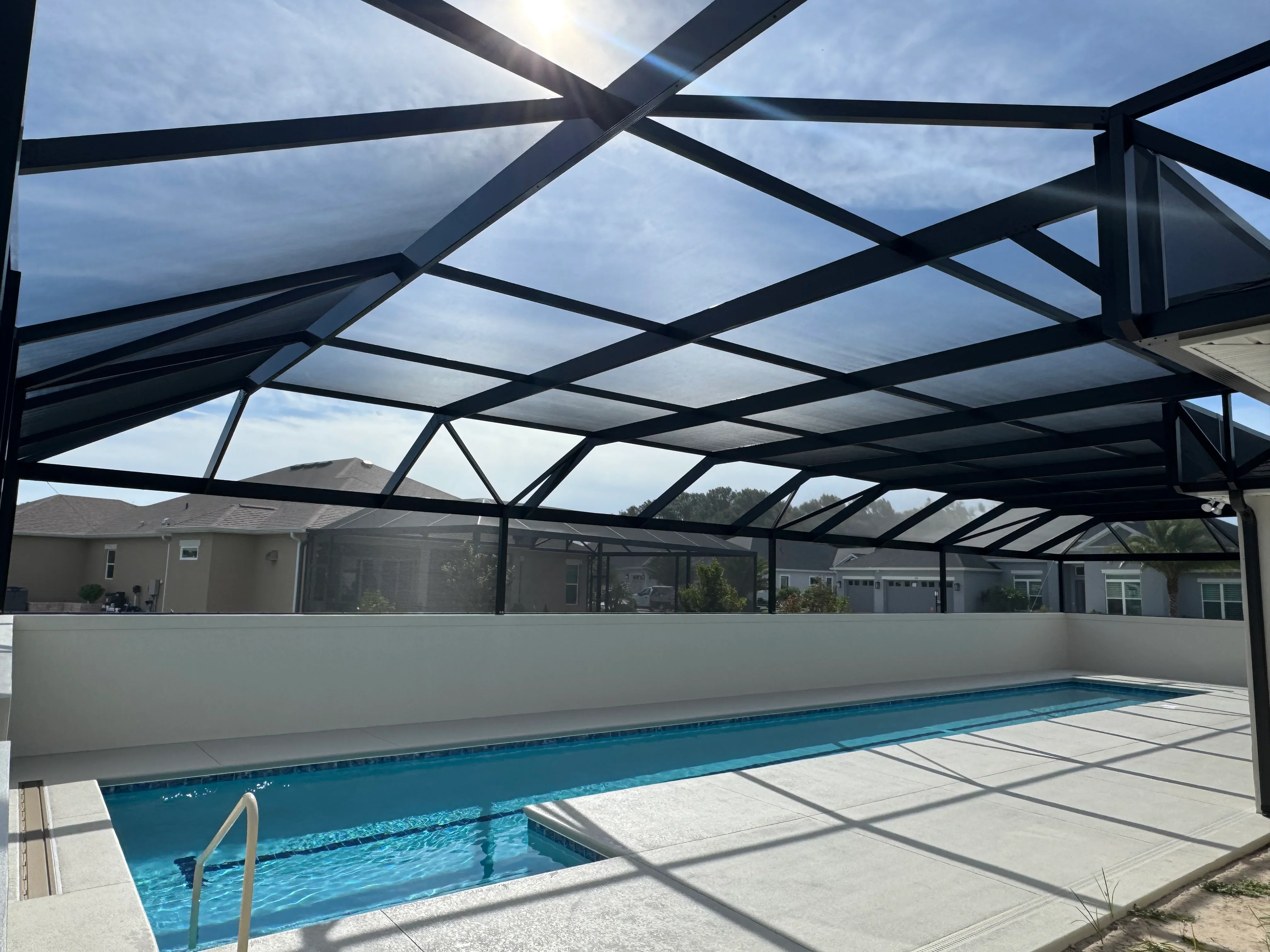 Black aluminum pool enclosure with clear glass panels over in-ground swimming pool and concrete deck