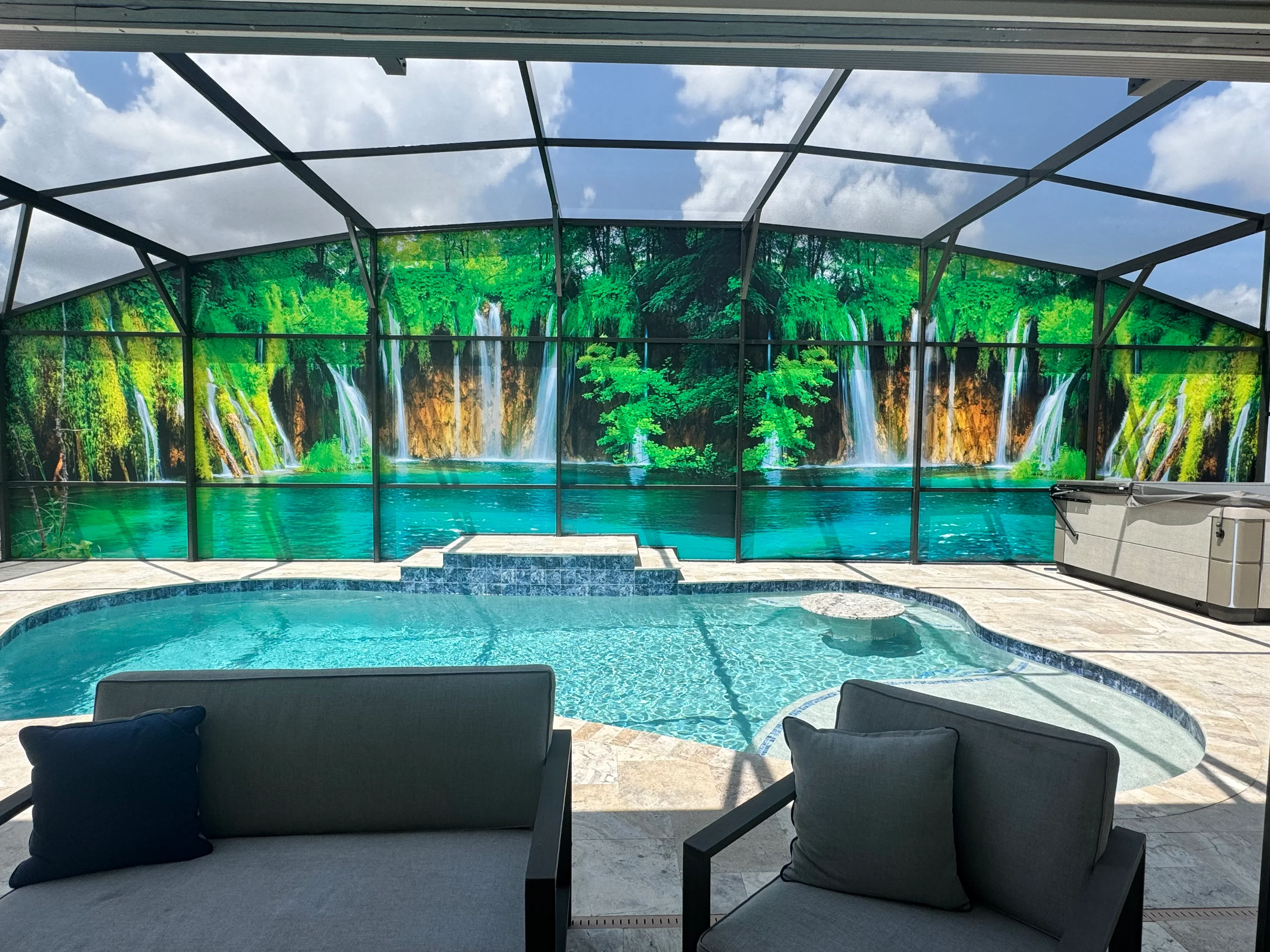 Black aluminum pool enclosure with screened panels and waterfall mural backdrop