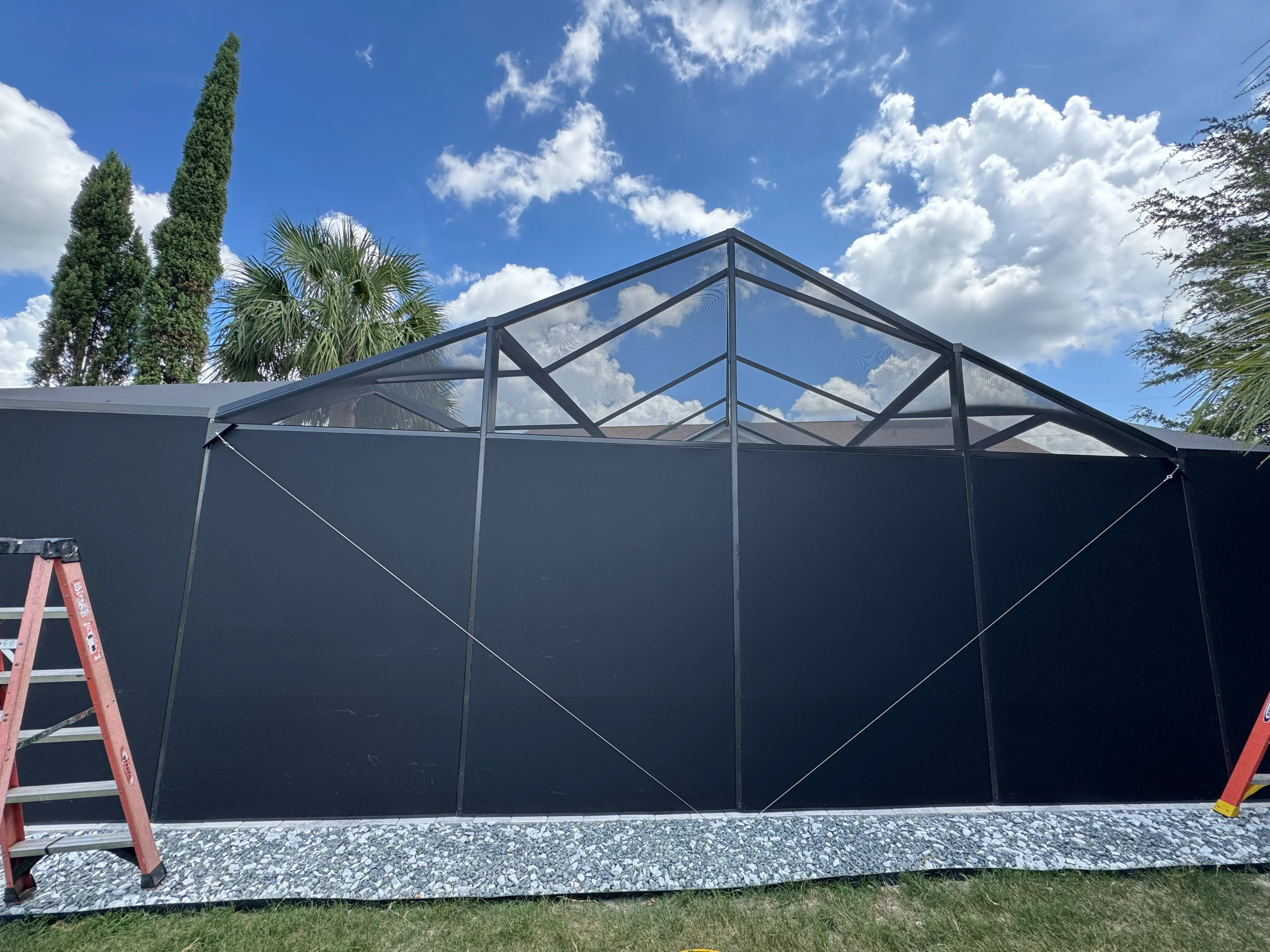Black aluminum screen enclosure with gable roof, mesh panels, and clear roof sections