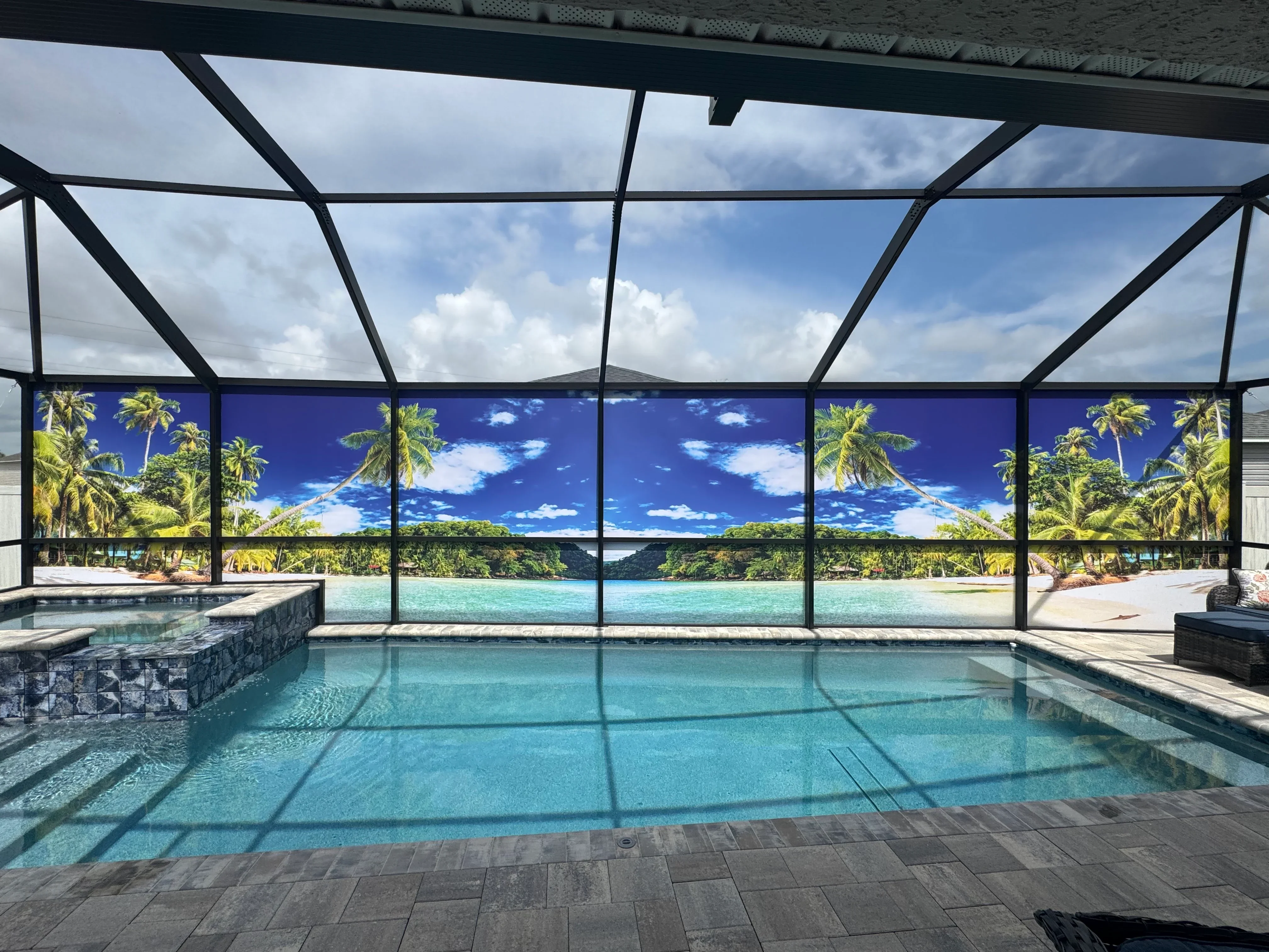 Large pool enclosure with black aluminum frame, clear glass panels, and screened walls overlooking tropical landscape
