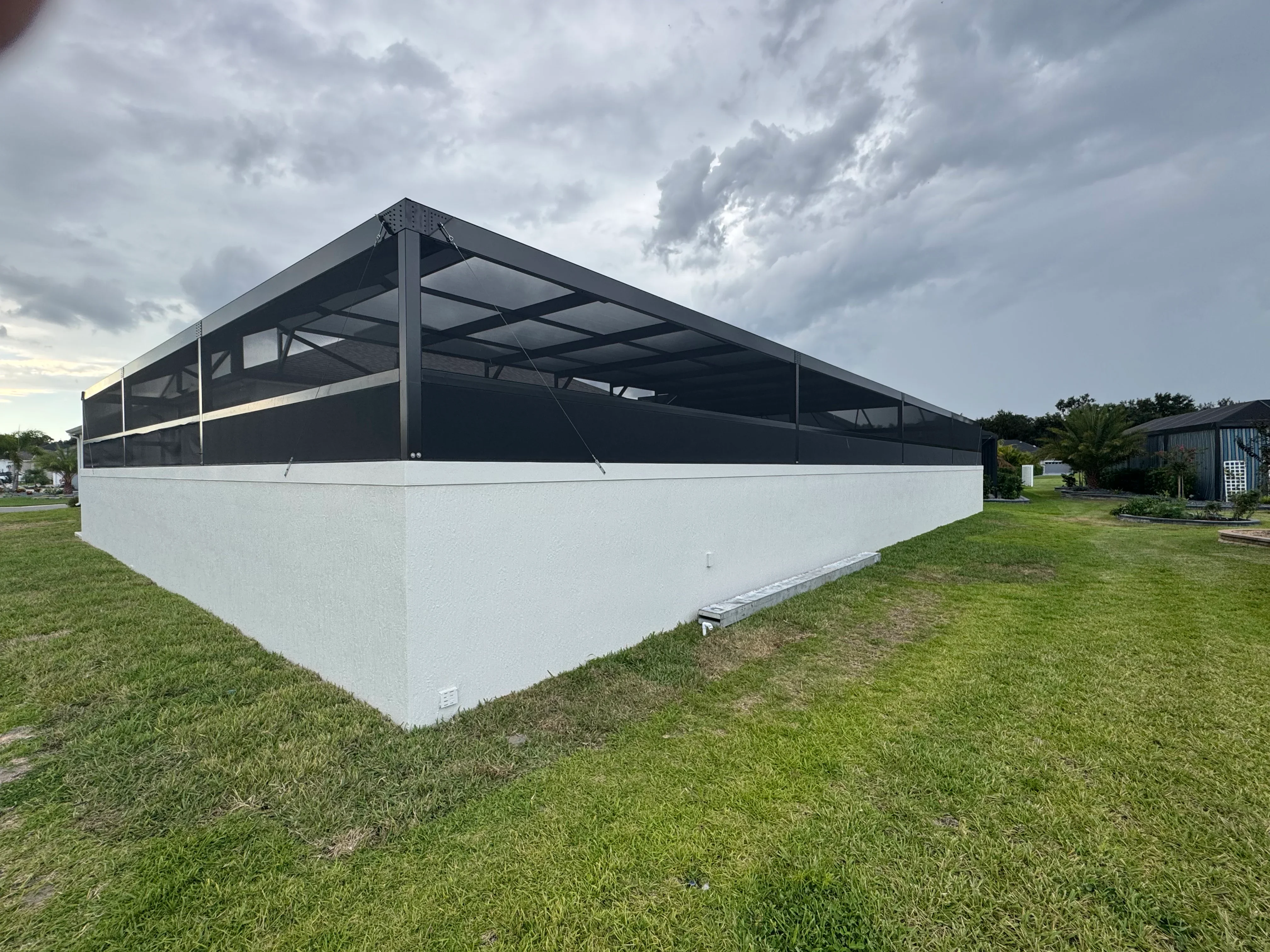 Steel-framed screen enclosure with black aluminum frame and mesh panels on white base wall