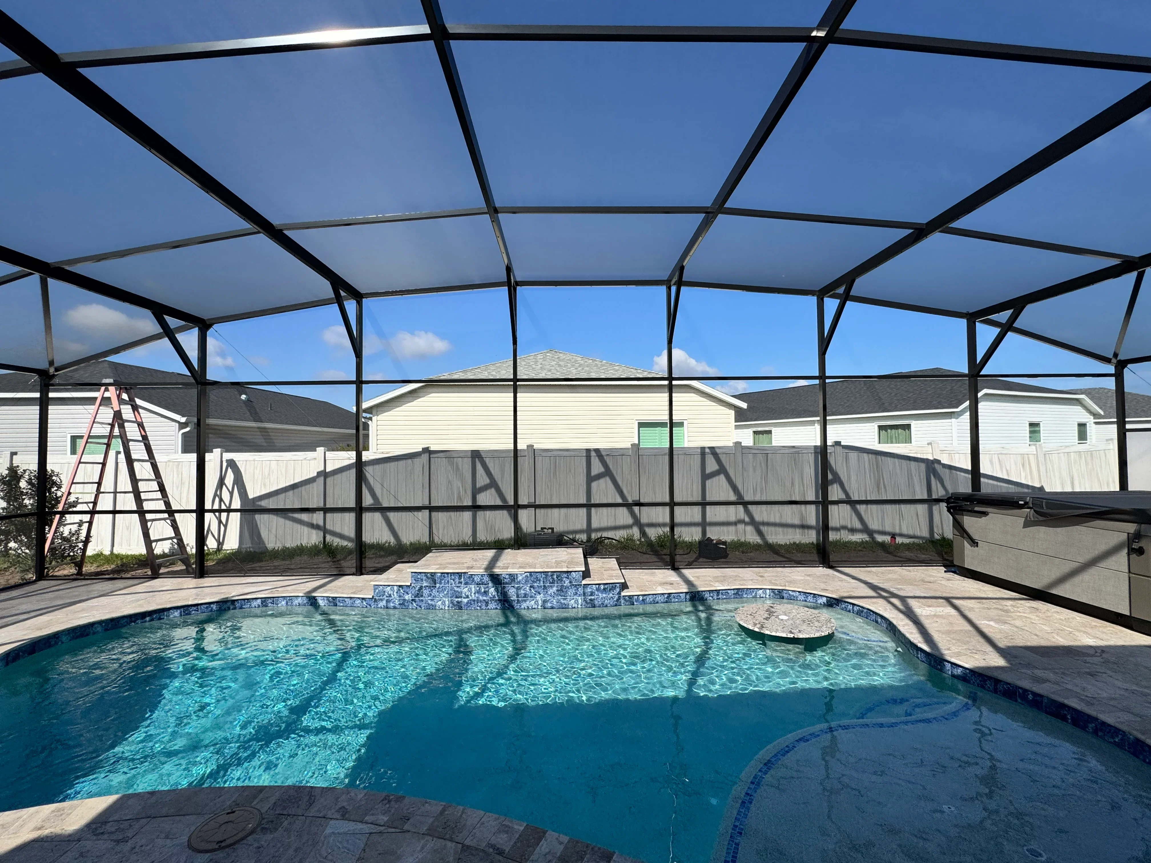 Black aluminum pool enclosure with clear screening over in-ground pool with spa jets and tile accents
