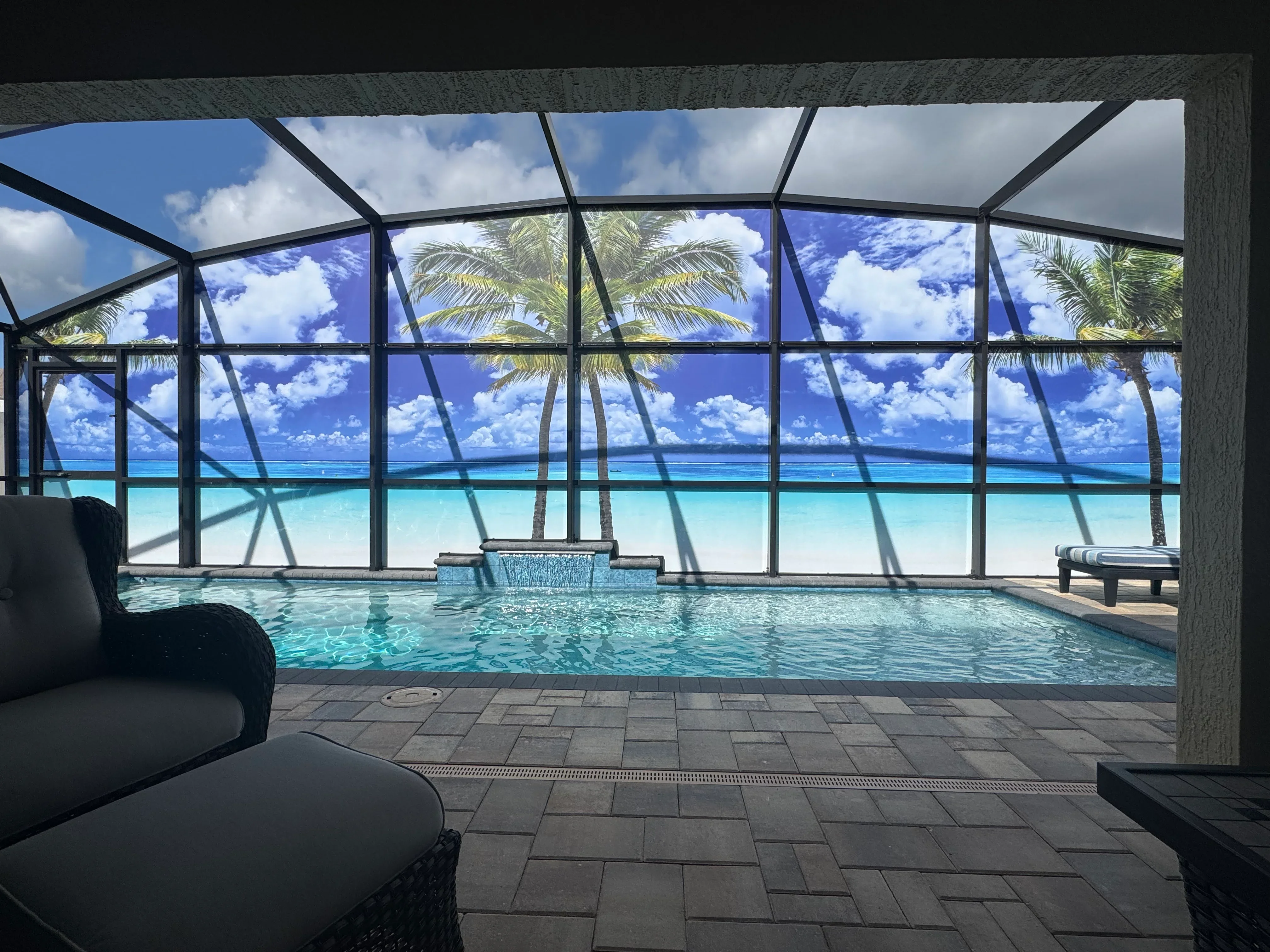 Black aluminum pool enclosure with glass panels overlooking ocean, paver deck, and integrated spa