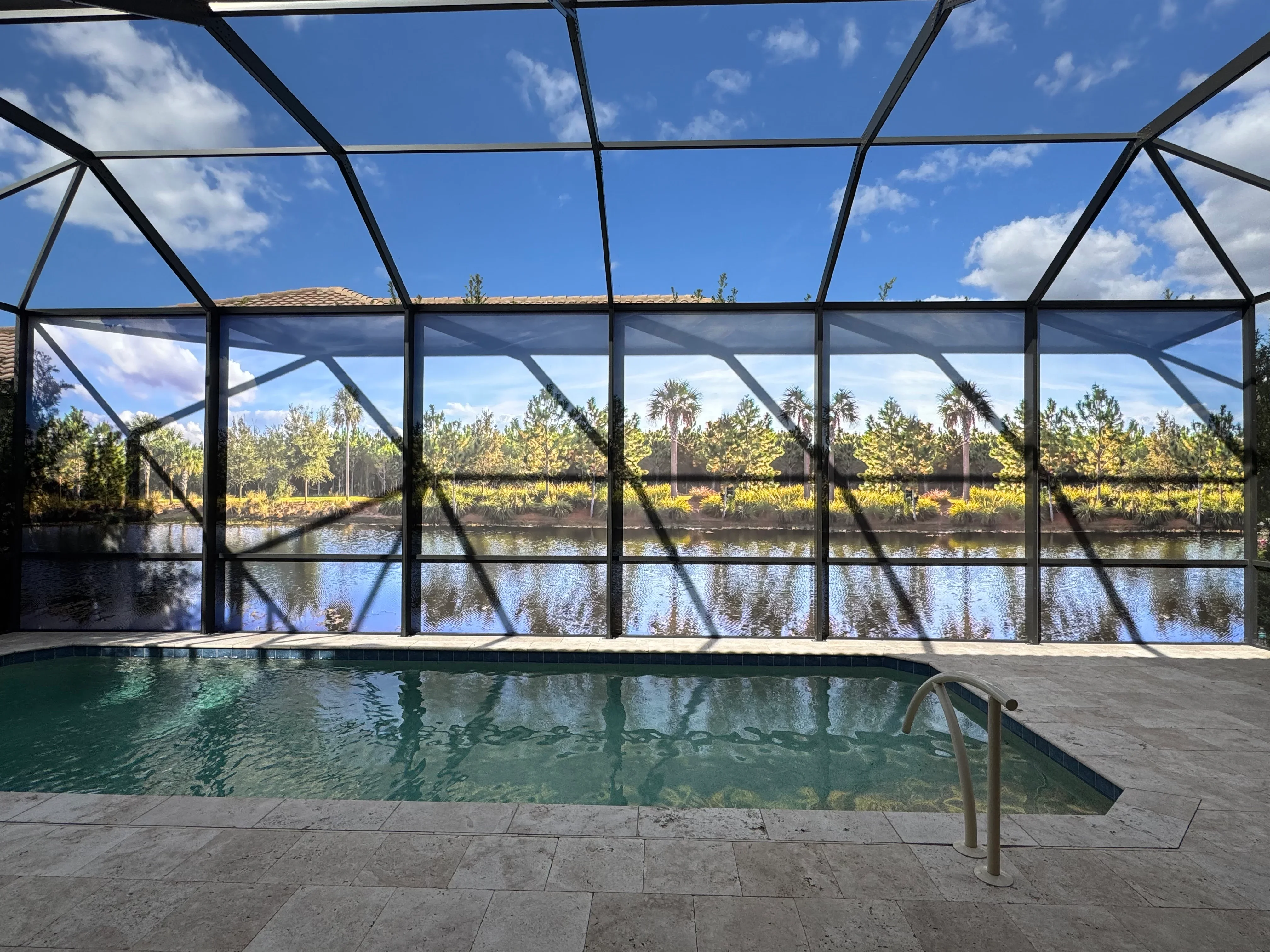 Black aluminum pool enclosure with glass panels and geometric roof framing overlooking water and trees