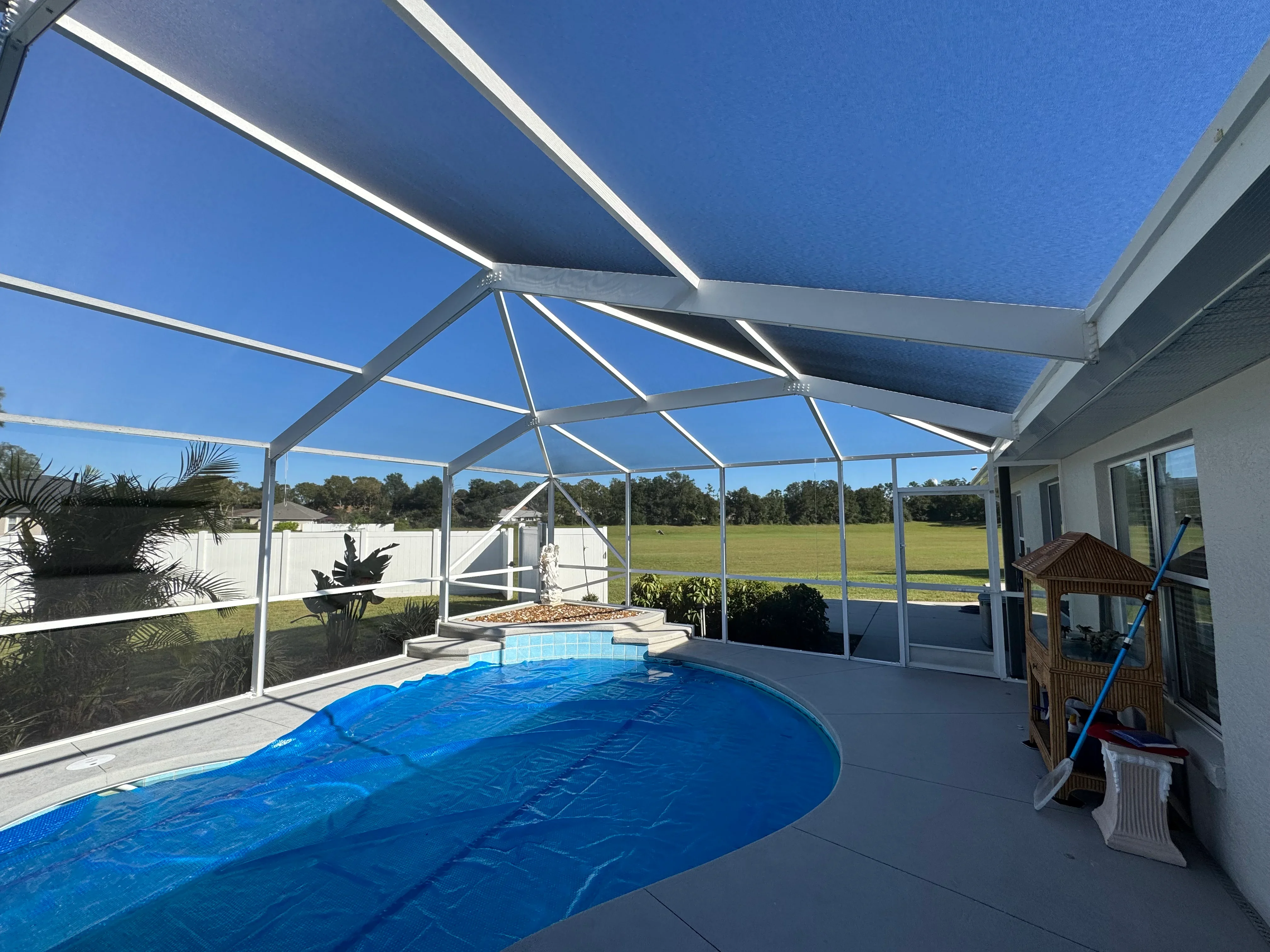 Aluminum pool enclosure with white frame and clear screening panels over in-ground pool