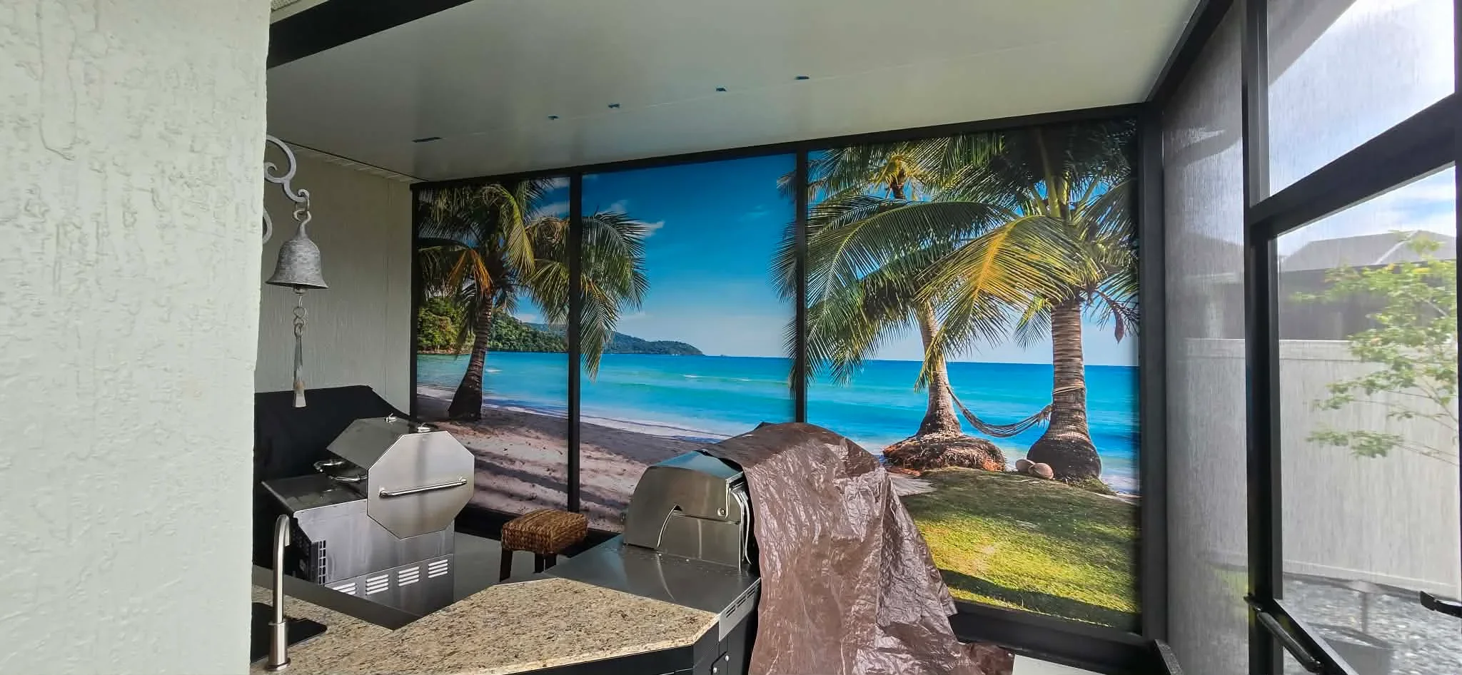 Large tropical beach mural screen with black aluminum frames and mesh panels in outdoor space