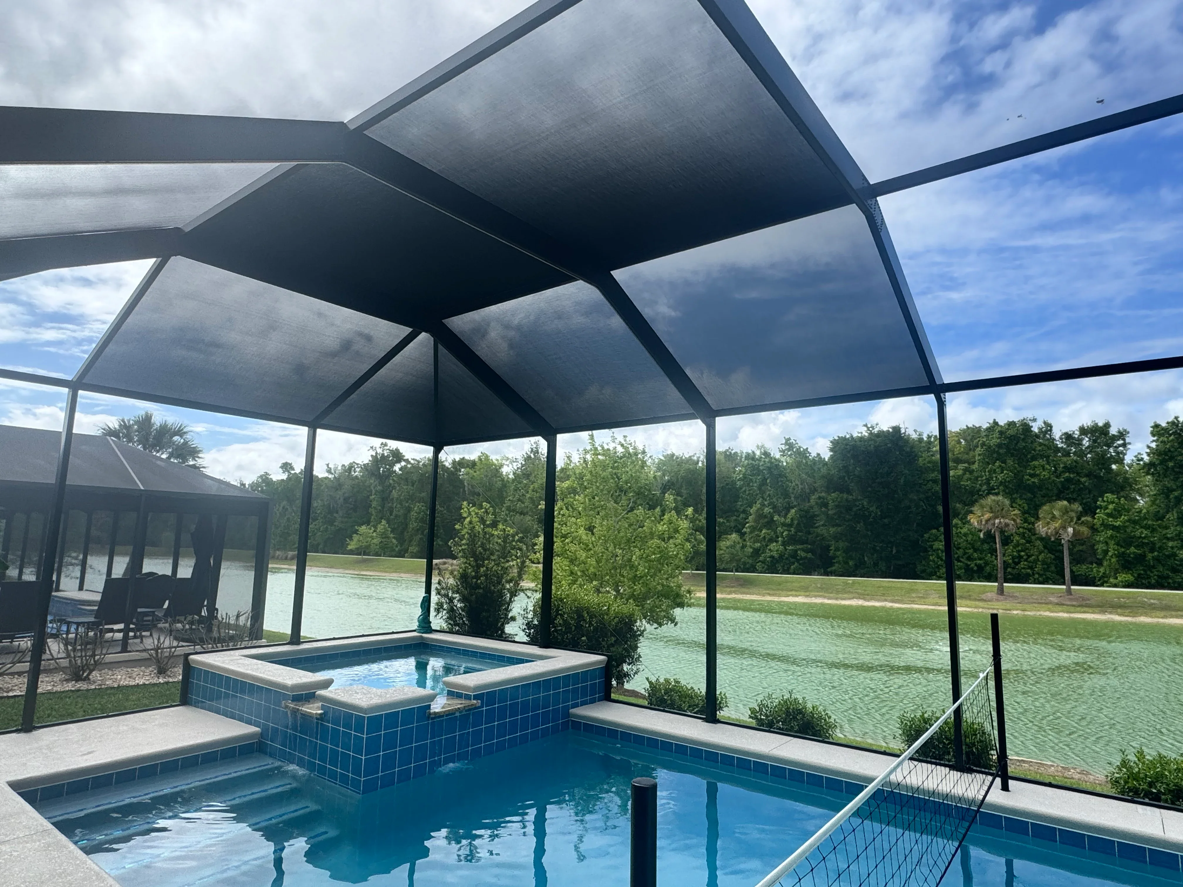 Motorized shade pool enclosure with aluminum frame, mesh screening, and blue tile spa and pool
