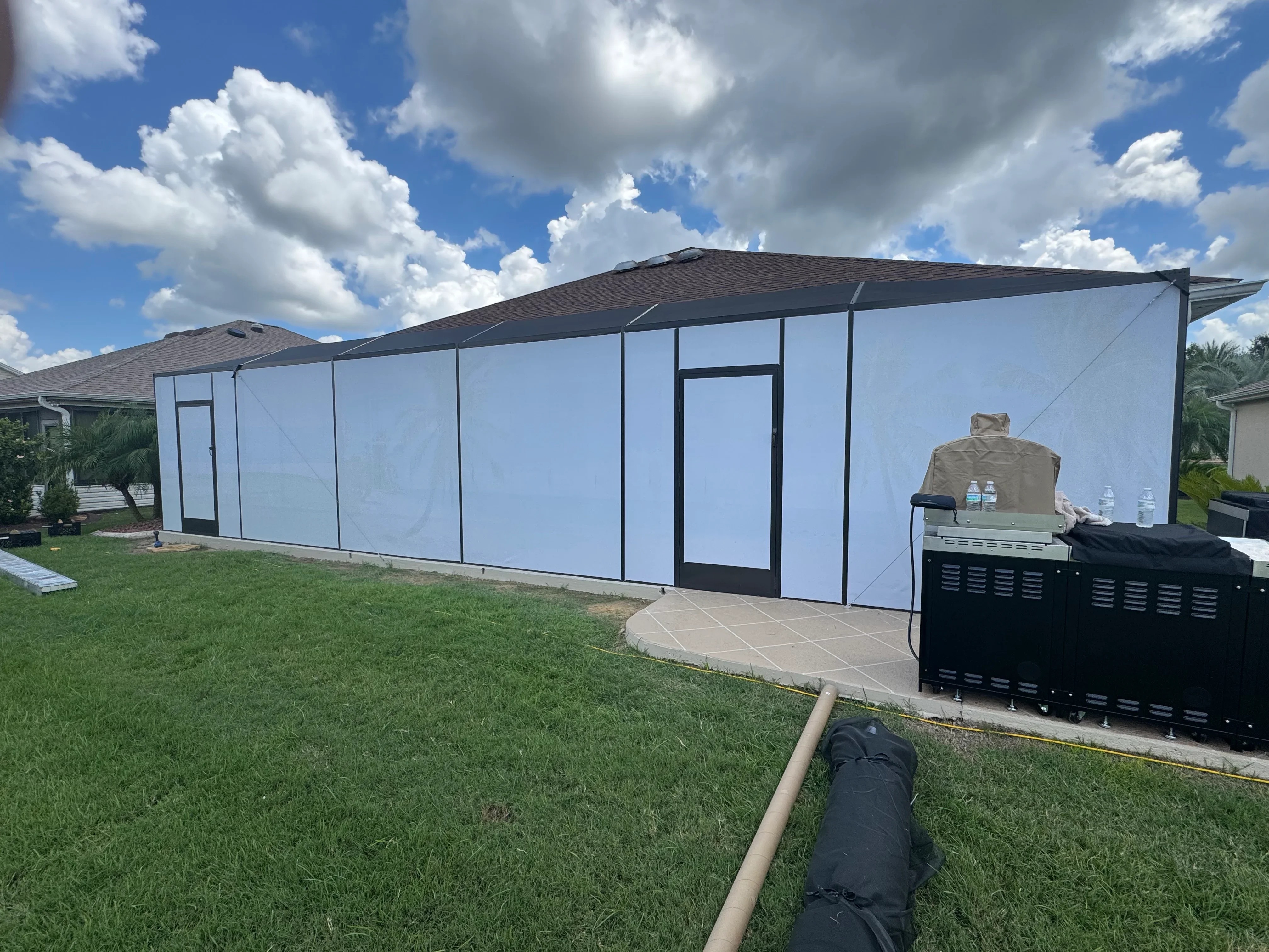 Black aluminum frame screen enclosure with blue mesh panels and dual doors on concrete pad