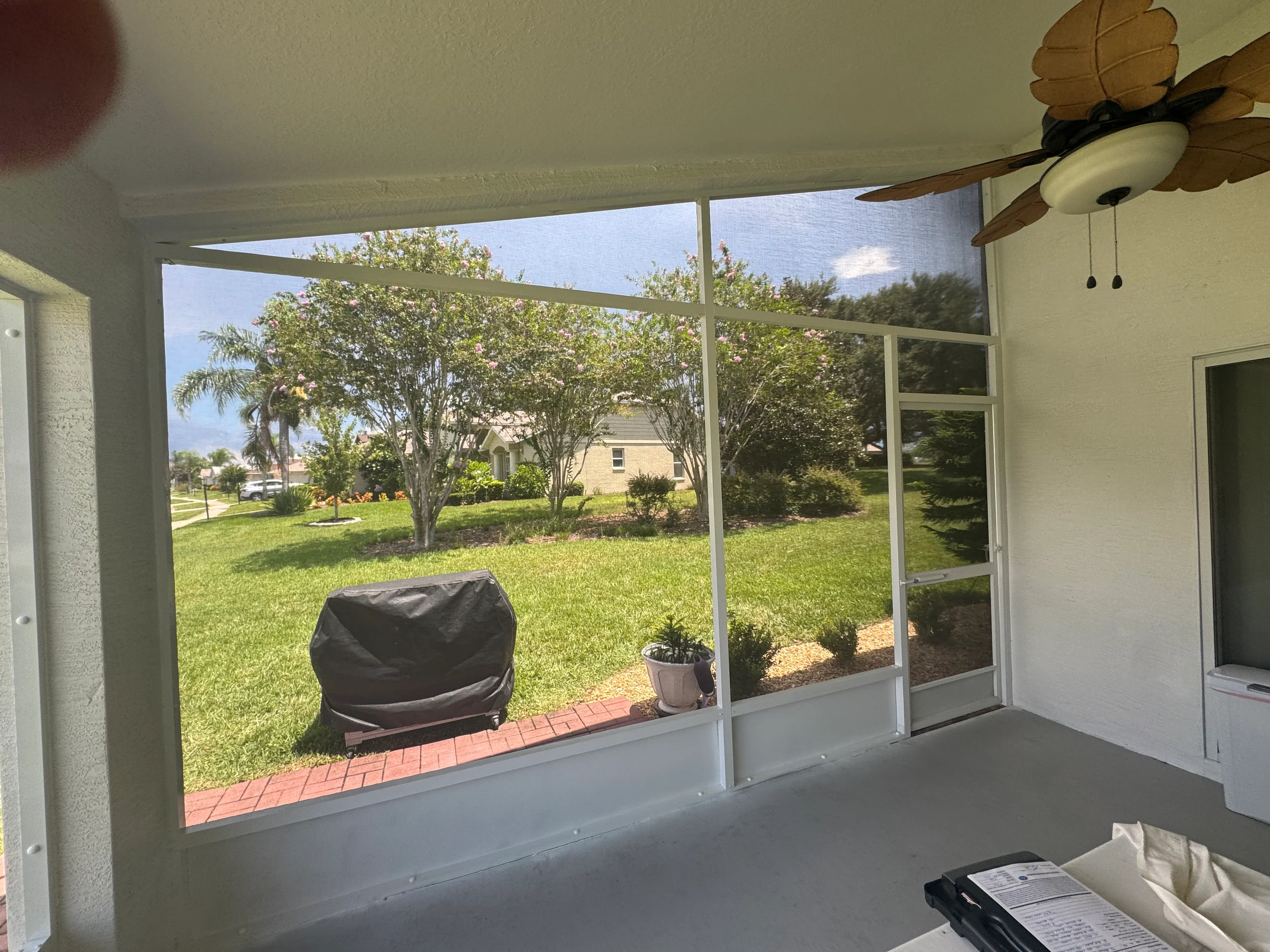 Aluminum framed lanai screen enclosure with white frame and clear panels overlooking brick patio and lawn